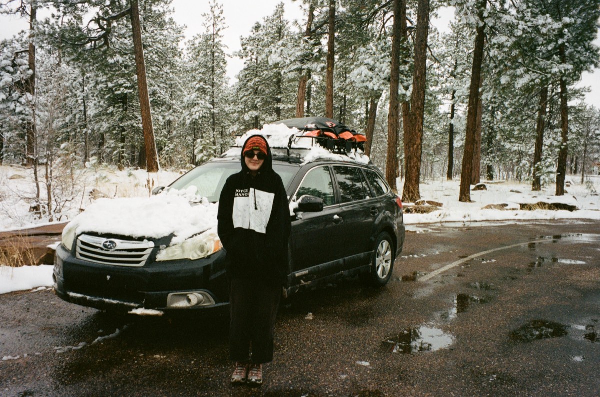 A snow-covered car with a loaded roof rack parked among the pines